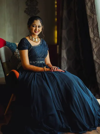 A seated portrait showing the beautiful drape of the blue georgette gown. The embellished belt and one-shoulder design add a touch of modern sophistication.