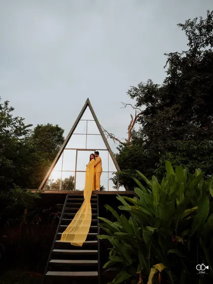 A wide shot of the couple in front of the A-frame house, emphasizing the dramatic architecture and natural surroundings.