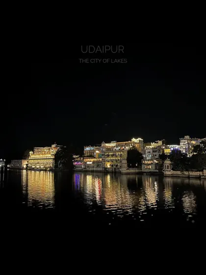 A night shot of the illuminated City Palace complex in Udaipur, reflecting in the calm waters of the lake.