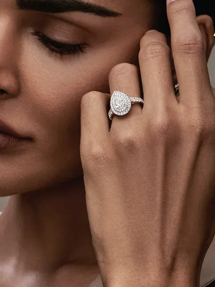 A detailed shot focusing on the hand and face for Aukera Jewellery. The makeup is minimal and skin-focused, with clean nails, ensuring the stunning pear-shaped diamond ring is the hero.