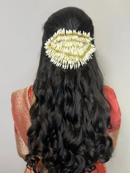 A beautiful example of a simple yet elegant hairstyle for a guest. The hair is styled in soft waves and decorated with a large, intricate jasmine flower arrangement.