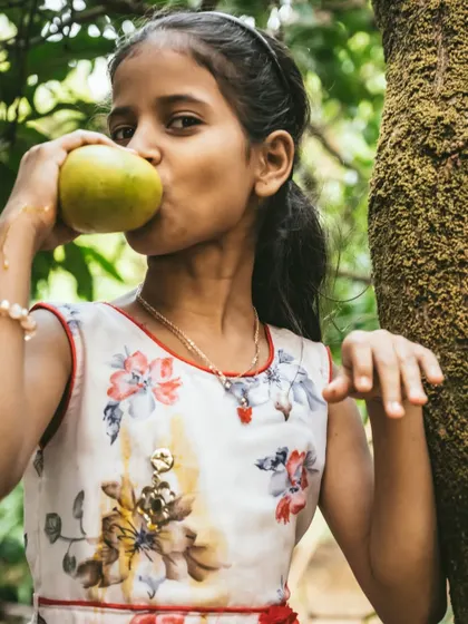 A young girl taking a big bite out of a fresh mango, a perfect capture of carefree childhood joy.