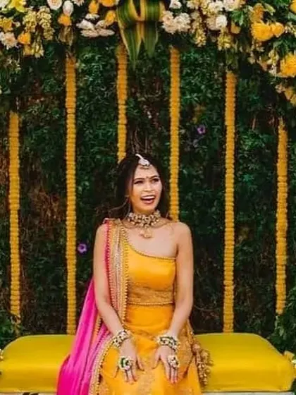 A happy bride enjoying her Haldi ceremony on a swing. The swing is placed under a lush arch of greenery and yellow flowers, creating a beautiful photo opportunity.
