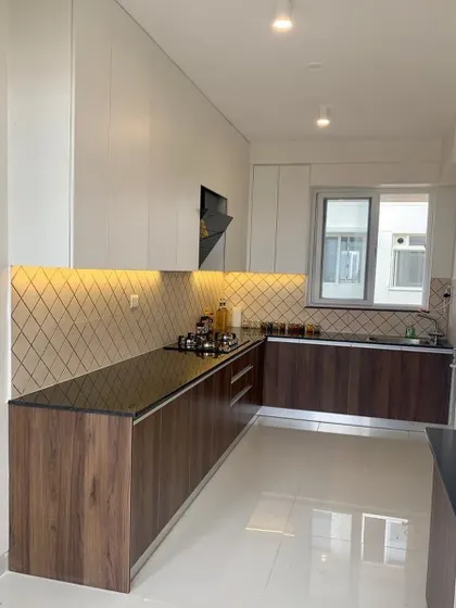 This L-shaped kitchen combines dark wood grain base cabinets with white upper cabinets. The diamond-patterned tile backsplash and under-cabinet lighting add a touch of subtle elegance.