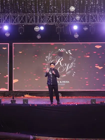 On stage with a large screen backdrop, commanding the attention of the audience. A professional emcee needs to have a strong stage presence to manage large-scale productions and keep the event flowing smoothly.