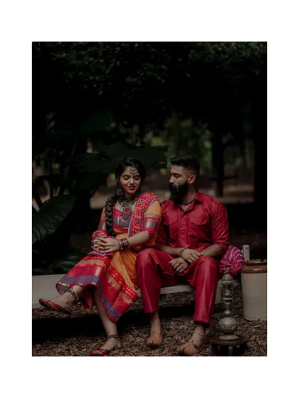 A moody and romantic portrait of a couple in colorful traditional wear, set against a dark, natural background that makes their attire pop.