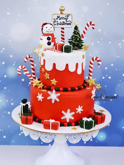 A bright red two-tier Christmas cake that captures the joy of the season. It's decorated with snowflakes, candy canes, edible presents, and a cheerful snowman topper.