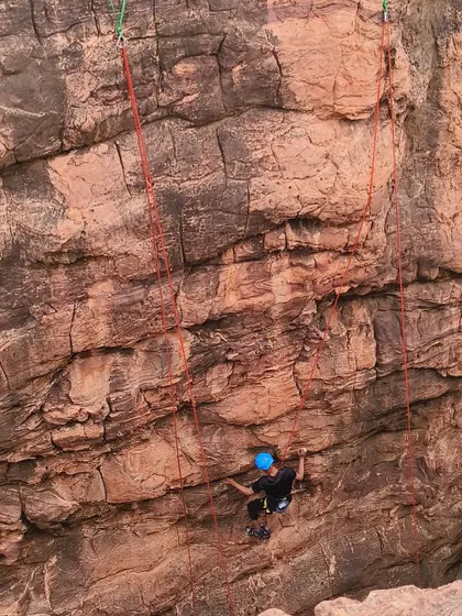 A lone climber scales a textured rock wall, highlighting the excellent grip and features of Badami's sandstone.