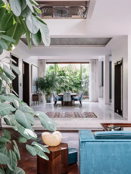 Peeking from the living area into the dining space, you can see how the different zones of the home are visually connected. The consistent use of white marble floors and abundant greenery creates a harmonious flow throughout the ground level.
