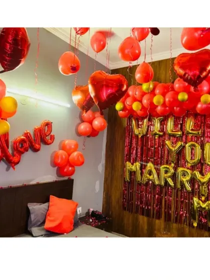 You can even plan a proposal right at home. This bedroom is decorated with "Will You Marry Me" and "Love" foil balloons, a shimmery curtain backdrop, and red heart balloons floating from the ceiling.