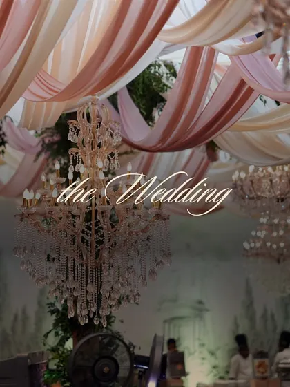 A close-up of the stunning crystal chandeliers hanging amidst draped pastel fabrics. The warm light from the bulbs creates a romantic and celebratory glow.