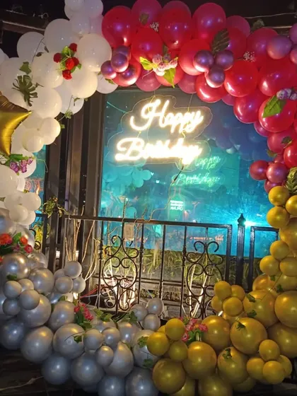 A beautiful ring arch decorated with red, white, and gold balloons, accented with small flowers. The neon sign against the window creates a lovely silhouette effect.