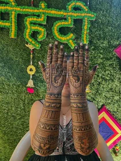 A happy bride showing her full bridal mehendi against the backdrop of her mehendi ceremony decor.