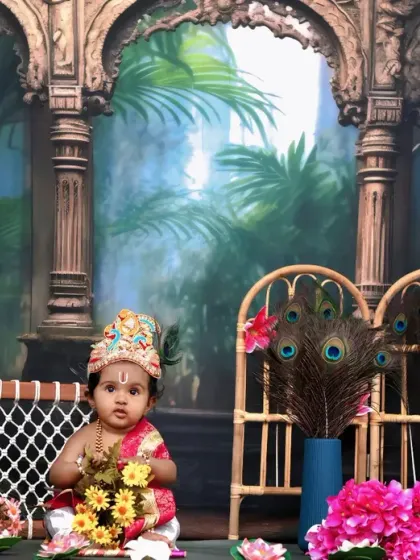 This wide shot captures the full splendor of our Krishna setup, with the baby sitting among flowers, greenery, and peacock decor.