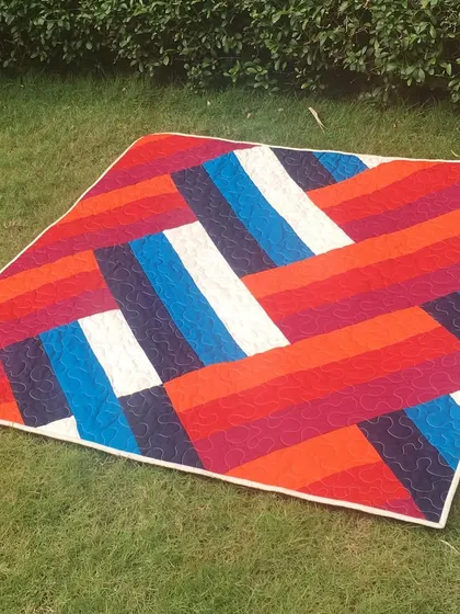 A modern quilt with a bold, striped pattern in vibrant reds, oranges, and blues.