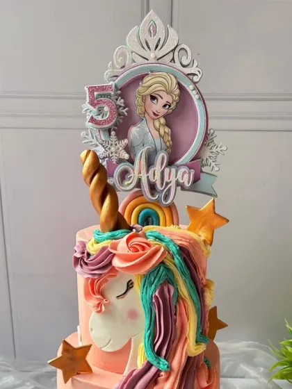 A magical mashup of Frozen and Unicorns. This handmade paper topper features Queen Elsa in a beautiful tiara design, sitting atop a colorful unicorn cake.