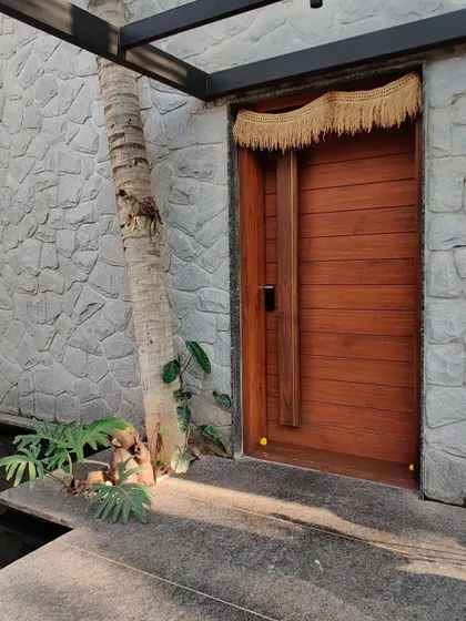 A slightly different angle of the entryway, showing the warm wooden door, the textured stone wall, and the existing coconut tree integrated into the design.
