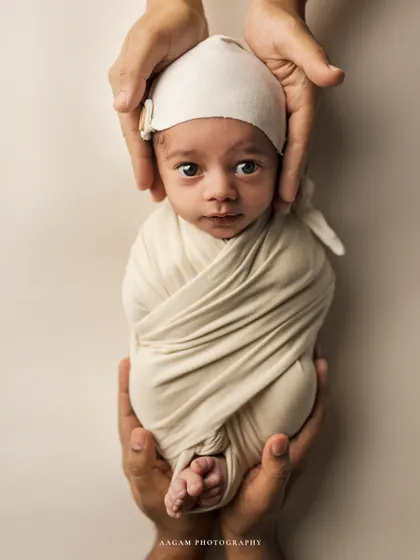 A close-up of a swaddled newborn's curious and alert expression, held securely by their parents. A beautiful portrait of a new life just beginning.
