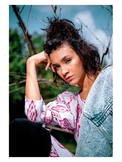 A high-fashion, editorial-style portrait taken outdoors. The composition and her pose feel like a page from a magazine, blending style with a natural setting.