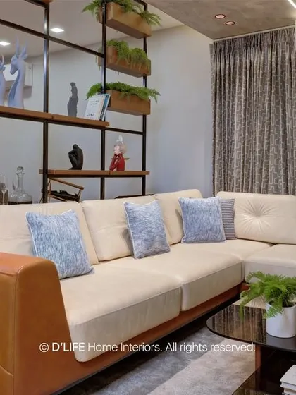 A detail shot of the living room's L-shaped sofa and the open shelving partition that separates the space while maintaining a visual connection to the dining area.