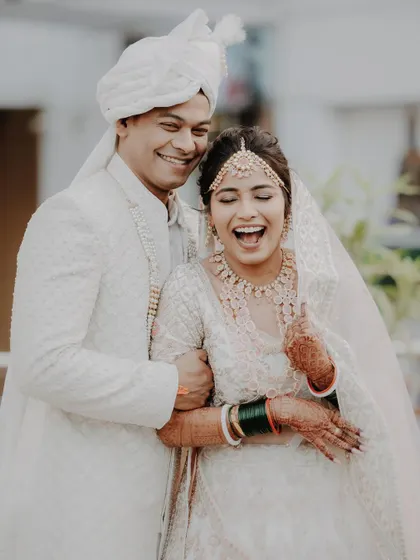 Pure joy. This candid shot captures the couple bursting into laughter, dressed in stunning all-white wedding attire. It's a moment of pure, unscripted happiness.