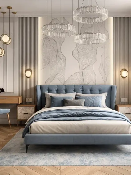 This bedroom combines a tufted blue headboard with modern crystal chandeliers and warm wood flooring. A small, integrated desk area makes the space functional for work without compromising its restful feel.
