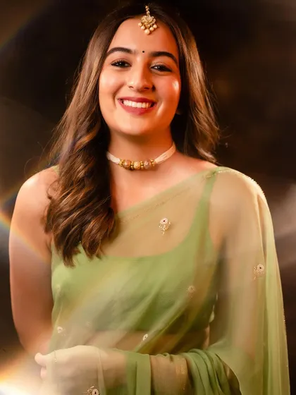 A soft and dreamy portrait with a subtle light flare effect. The gentle lighting and the subject's happy expression create a warm and inviting image, highlighting the delicate green saree.