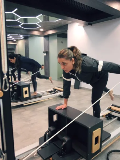 This client is performing a single-leg plank on the Reformer, a move that challenges balance and deeply engages the core muscles. The mirror reflection shows her focused alignment.