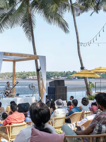 An overview of the beachside 'Sitar for Mental Health' session in Goa, showing guests relaxing in a beautiful, natural setting.