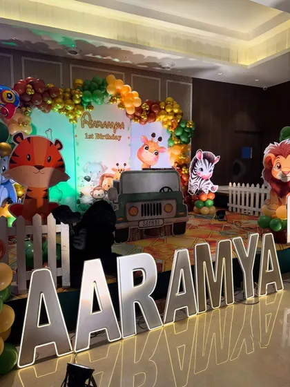 The complete jungle birthday stage with marquee letters spelling "AARAMYA" brightly lit in the foreground.