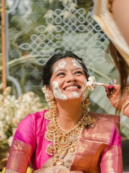 The bride looks up with a wide, happy smile as haldi is applied. This is a moment of pure bliss and anticipation, beautifully captured in the South Indian themed ceremony.