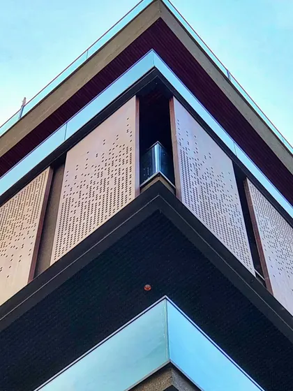 A corner detail of a building facade, showing perforated metal screens. These screens provide privacy and solar shading for the balcony while adding a decorative, high-tech element to the exterior.
