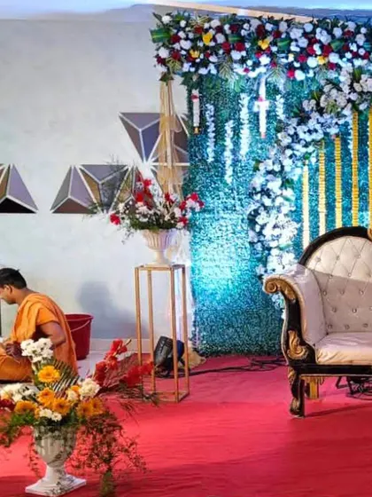 A beautiful blend of natural and modern elements. This stage features a lush green wall backdrop with white floral cascades, paired with a classic white and gold sofa for the couple.