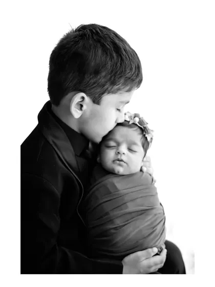 A touching black and white photo of an older brother gently kissing his newborn sister's forehead. This captures the beginning of a lifelong sibling bond.