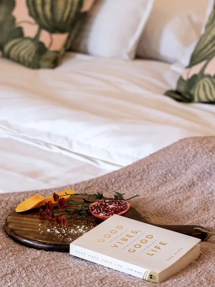 A cozy bedroom scene with a book titled "Good Vibes, Good Life" resting on a wooden tray with fresh fruit. This image perfectly captures a mood of relaxation, positivity, and self-care.