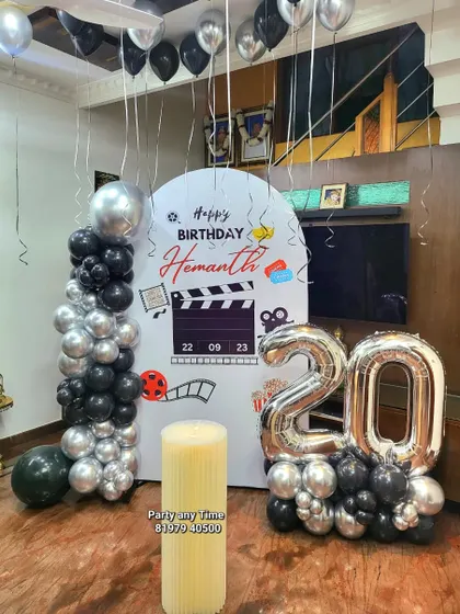 A movie-themed 20th birthday party with a custom clapperboard backdrop and a black and silver balloon arrangement.