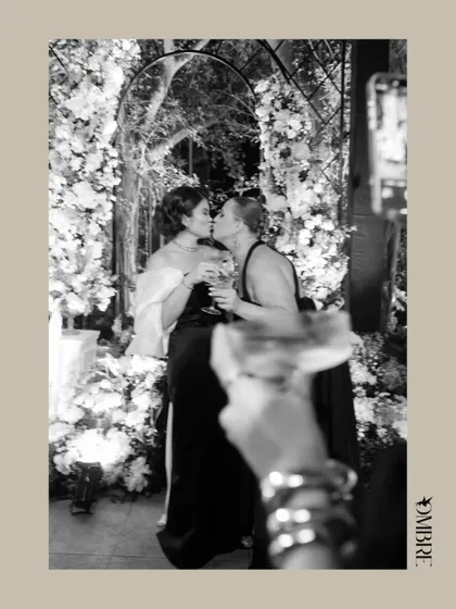 A sweet, black and white photo of the bride-to-be sharing a kiss with a friend, celebrating under a floral arch.