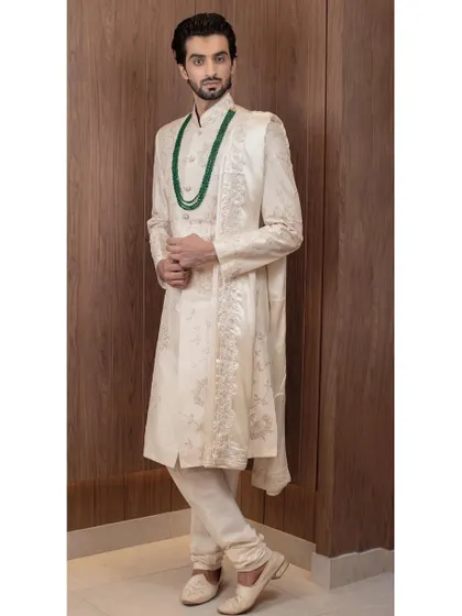 A closer look at the fine craftsmanship of our ivory sherwani, paired with an emerald green mala. This combination of classic ivory and rich color adds a touch of personal style to traditional groomswear.