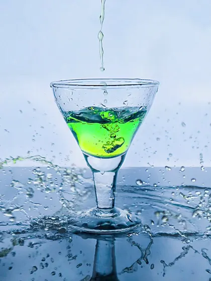 A green drink being poured into a glass, with water splashing up around it. This action shot is full of energy and gives a sense of ultimate refreshment.
