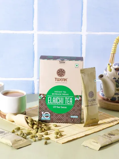 This image for Elaichi Tea is set against a kitchen tile background, giving it a fresh, morning feel. The traditional teapot and scattered cardamom pods reinforce the authentic flavor.