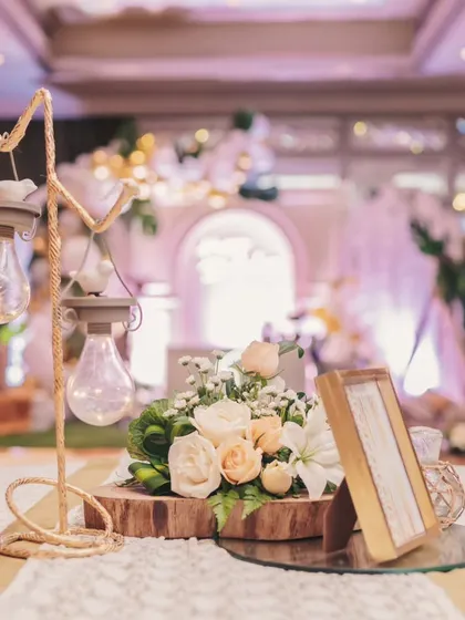 A rustic centerpiece combining a wooden slice, a unique light fixture, and a fresh floral arrangement of white and peach roses, perfect for the elegant jungle theme.