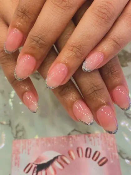 A subtle and chic design featuring a sheer pink base on natural-looking oval nails. A thin line of silver glitter along the tips gives a modern update to the classic French manicure.