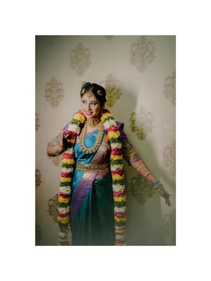 A full-length shot of the bride in her stunning blue saree and vibrant garland, capturing a moment of happy movement.