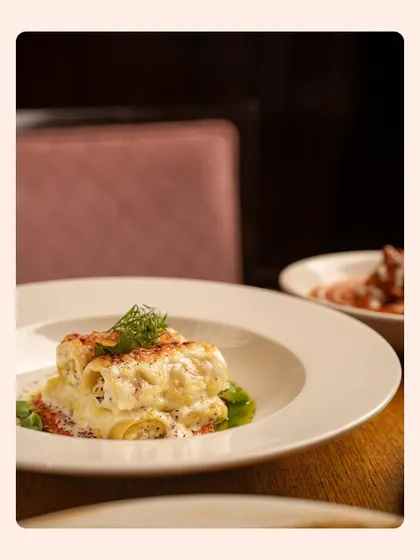 Creamy cannelloni captured in a cozy, low-light restaurant environment. This style of moody food photography is ideal for creating an upscale and intimate atmosphere for fine-dining establishments.