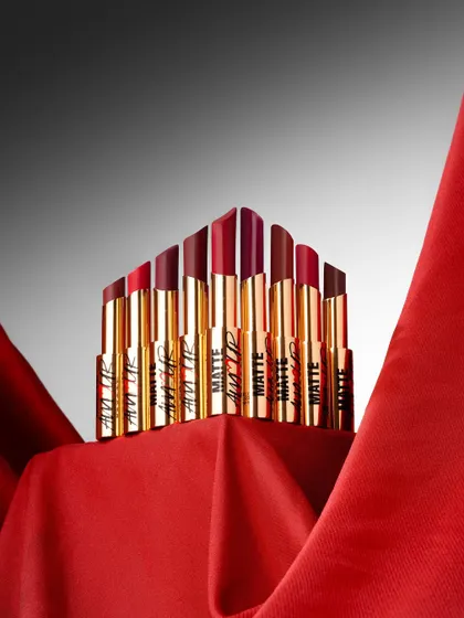 A powerful product shot that arranges these matte lipsticks into a crown-like formation. The dramatic lighting on the rich red fabric creates a sense of luxury and desire, perfect for a beauty brand campaign.