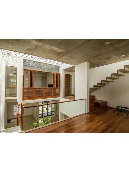 An interior view of 'Cube Square', where the open-plan design is organized around the central courtyard. The staircase and bridge on the upper level create dynamic viewpoints, while the exposed concrete ceiling adds a raw, textural quality to the space.