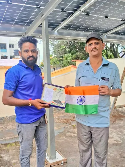 Our team member presents a certificate to a proud new solar homeowner holding the Indian flag.