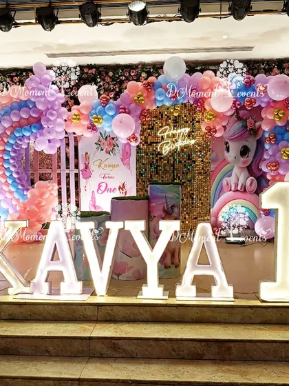 A whimsical unicorn and rainbow stage setup for a first birthday, featuring a sequin backdrop, a large unicorn figure, and a beautiful balloon rainbow arch.