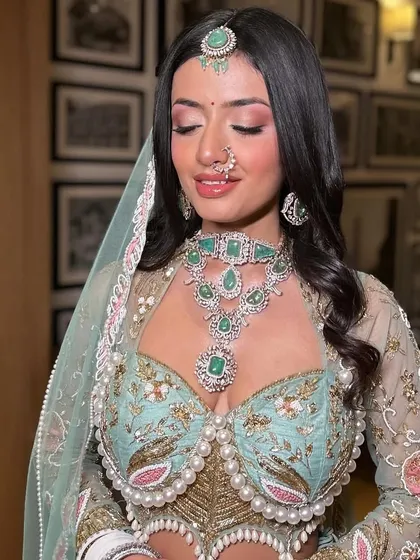 This bride's fresh, radiant day look is perfect for a modern wedding. The soft pink eyeshadow and glowing skin complement her pastel lehenga and emerald jewelry beautifully.