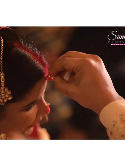 The sindoor daan, a pivotal and symbolic moment in a Hindu wedding. This tight close-up focuses on the groom's hand as he applies the sindoor, capturing the intimacy of the ritual.